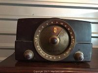 Front view of vintage Zenith radio showing large circular dial with AM/FM frequency markings, speaker grille, and two tuning knobs.