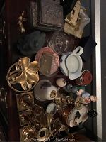 Brass candlesticks, assorted decorative items including switch plates, figurines, and boxes on a dark surface