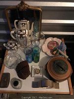 Wide-angle view of various decor and vintage items on a white tabletop, including teapots, glasses, pottery, clocks, and decorative accents.