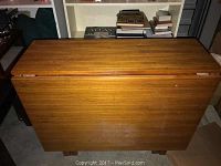 Folded drop leaf table showing top horizontal wood grain surface and legs underneath in storage position.