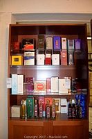 Four-tier wooden shelf with assorted boxed perfumes on upper shelves and bottled oils on bottom shelf