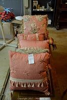 Multiple decorative pillows arranged on a table, displaying various sizes and styles primarily in pinks with embroidery and tassels.