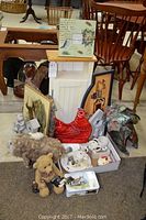 Small wooden shelf cabinet with white door and multiple decor items arranged around it including rooster figurine, cushions, tea cozy, sheep figurine, teddy bear figurine, photo frame and antique sign.