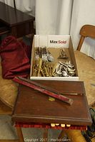 Tray with assorted knives, forks and spoons, wooden chest with red lining, and red pillow shams arranged on a wood table.