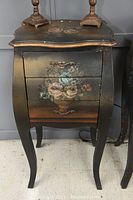 Front view of the black decorative end table showing the three drawers with floral painted designs and curved legs.