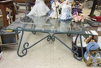 Photo of metal framed coffee table with clear beveled glass top, displaying curled legs and decorative metalwork below the glass surface.