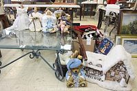 Full view of Christmas decorations on glass table and surrounding floor area, showing nativity figures, house scene, teddy bear figurine, and various holiday decorations.
