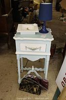 Ornate painted table with drawer, purses underneath, and blue lamp on top