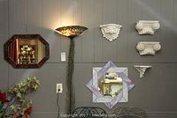 Wide view showing octagonal mirror, stained glass wall light, plaster wall shelves, and square stained glass mirror on gray wall.