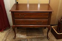 Front view showing two drawers, one drawer missing two handles, lightly worn wood surface, cabriole legs and scalloped apron detail.