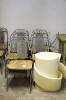 Set of five metal chairs with plywood seats and rolled foam for seat replacement, arranged in storage space against a wall.