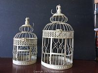 Front view of two decorative hanging bird cages showing their ornate metalwork and size difference.