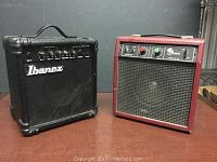 Front view of two amplifiers: black Ibanez and red Pascal on a wooden table