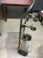 Side view of Milwaukee hand truck dolly cart showing large pneumatic tires and caster wheels, metal frame and baseplate with visible wear.
