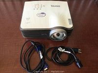 Top view of BenQ MX810ST projector with power cord and VGA cable laid out beside it on wooden surface.