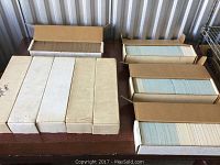 Nine boxes filled with baseball cards on a table, showing open boxes revealing tightly packed cards.