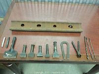 All tools laid out on a table with the railroad rail at the back and the chisels, drill bits and pliers in front.