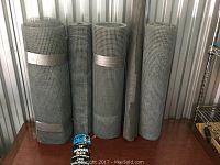 Five rolls of galvanized hardware cloth wire mesh on a table with gray color and fine square grid pattern