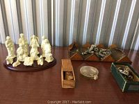 Ceramic nativity figurines arranged on a wooden base next to boxes of metal sewing attachments and tools on a wooden surface.