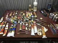 Full set of oil and acrylic paint tubes laid out on tabletop with brushes and tools arranged