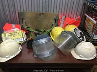 All safety gear items arranged on a table including five hard hats (three white, two yellow), two face shields, two orange safety vests, one green lanyard, and a red Sky Genie item.