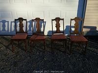 Four antique wooden dining chairs with carved backs and reddish brown upholstered seats, shown outdoors in front of a white garage door.