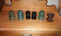 Full lot of six railway insulators on wooden surface showing variation in colors and styles.