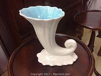 Photo showing cream-colored flared vase with curled base and blue interior glaze on a wooden table.