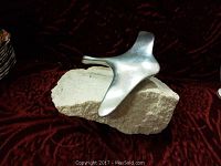 Front view of silver-toned cast aluminum goose figurine mounted on rough natural stone base on red fabric background.