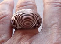 Close-up image of a silver domed ring worn on a person's finger, showing concentric circular grooves on the dome surface.