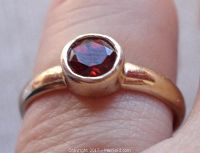 Close-up front view of the gold washed sterling silver ring with round garnet stone on finger.