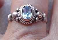 Front view of the ring on a hand showing the oval blue topaz set within a bezel and the detailed beaded silver design around the stone and along the band.