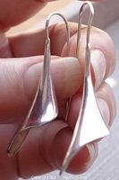 Close-up image of one earring held in hand showing twisted petal shape with shiny/brush finish and sterling mark.