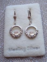 Front view of vintage sterling silver Claddagh pierced earrings showing the detailed design and lever-back hooks, placed on a beige soft display pad labeled 'Sterling Silver'.