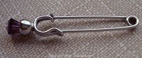 Full side view of the metal safety pin with purple faceted stone on top shaped like a thistle.