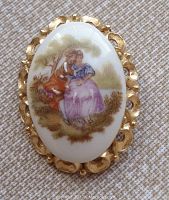 Front view of the oval Limoges porcelain brooch showing the romantic pastoral courting couple scene and gold-tone decorative frame.