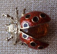 Close-up of the ladybug brooch showing the red enameled wings with black circles, orange glass body, clear rhinestones on the thorax, and green eyes.
