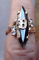 Front view of the ring showing marquise faceted black stone, gold letter B, and clear accent stones.