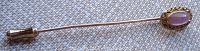 Full length side view of the stick pin showing the entirety of the pin with the end guard and decorative top with pink stone.