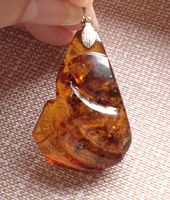 Close-up front photo showing translucent amber pendant with deep inclusions and silver bail against a textile background.