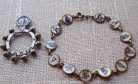 Photo of enameled religious link bracelet and Ave Maria rosary ring on fabric background.