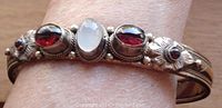 Close-up of the bangle on wrist showing garnet and moonstone settings with floral motifs and wire detailing.
