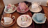Six vintage cups and saucers displayed on a table with assorted floral and gold-accented designs showing variety in pattern and colors