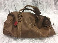 Exterior barrel-shaped duffle bag in brown leather with dual top handles and red leather tab.
