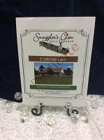 Photo of the $100 gift certificate for Smugglers Glen Golf Course on a black metal display stand surrounded by decorative stones.