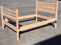 Photo shows a double extra long sized bed frame built in Mission style using red oak and roasted poplar accents, with horizontal slat headboard and footboard, placed outside on pavement.