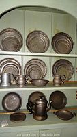 Full view of shelves with Wilton Armetale plates, pitchers, bowls, kettle, showing arrangement and condition.