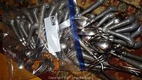 Plastic bag holding multiple pieces of Wilton Armetale flatware including forks, spoons, and serving utensils with ornate handles and visible corrosion.