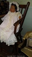 Photo of vintage Lee Middleton doll seated on antique wood youth chair, showing doll in lace gown and bonnet.