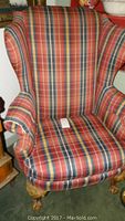 Front view of the wingback chair showing red and blue plaid upholstery and carved wooden legs.